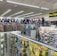 A well-lit store interior filled with fishing and outdoor equipment. The shelves are stocked with various lures, fishing lines, and other accessories. A range of colorful life vests is displayed on the back wall. A caution sign and a digital temperature display are mounted near the ceiling.